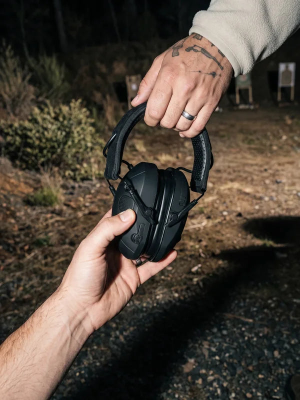 One shooter hands the folded VX1 PRO to another at an outdoor range at dusk